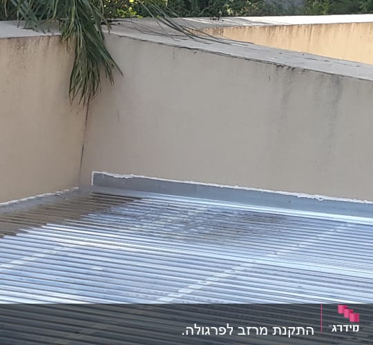 גג מתכת גלי ליד קיר בטון עם צמחייה